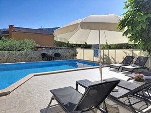 Une piscine entourée de chaises longues et d’un parasol, le tout bordé de murs en pierre et d’un bâtiment en pierre.