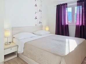 A neatly made bed with white linens, a bedside lamp, and a window with purple curtains. - Apartment Gorica 2 No.9 - with Balcony and Pool (Baska)