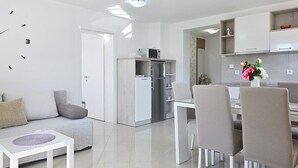 A modern kitchen with white cabinets, a microwave, and a refrigerator. There is a dining area with a white table and chairs. - Apartment Gorica 2 No.4 - with Balcony and Pool (Baska)