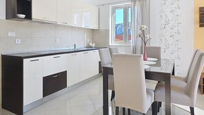 A modern kitchen with white cabinets, a black countertop, and a dining area with a table and chairs. - Apartment Gorica 2 No.7 - with Balcony and Pool (Baska)