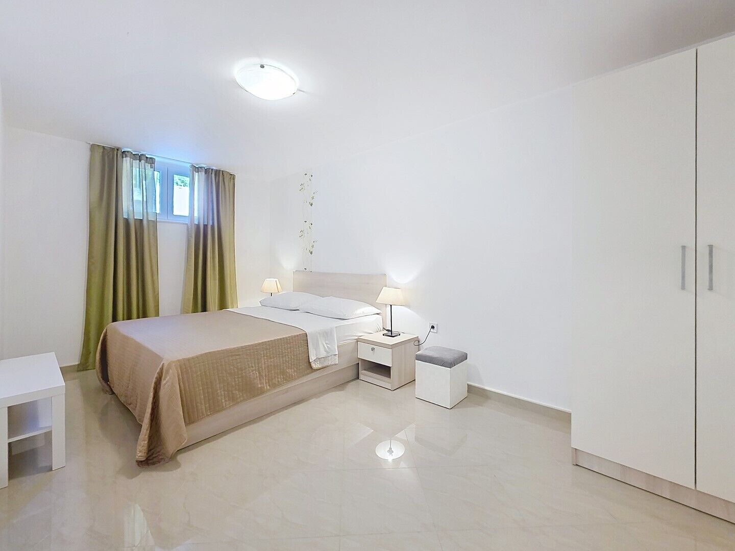 A bedroom with a bed, bedside tables, a nightstand, a wardrobe, and a window with curtains.