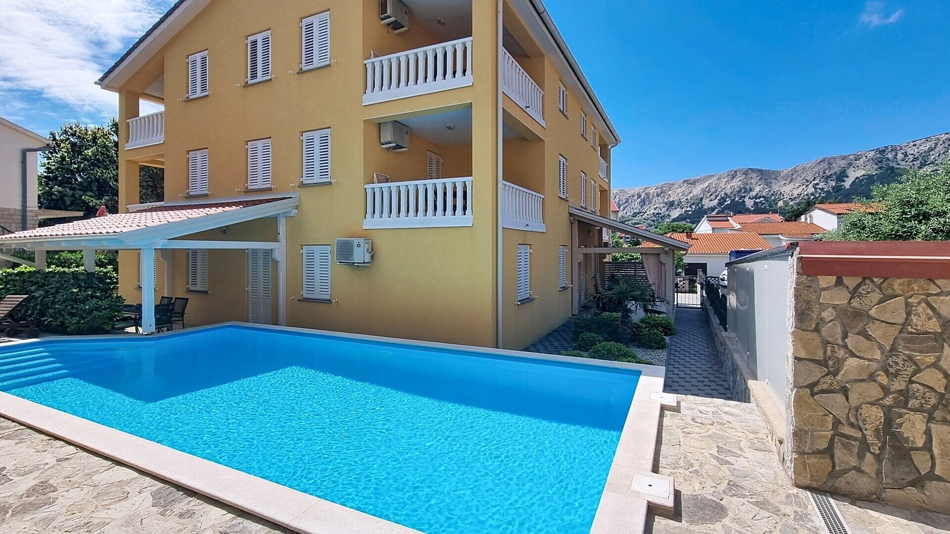 A building with a swimming pool, balconies, and a mountainous backdrop.
