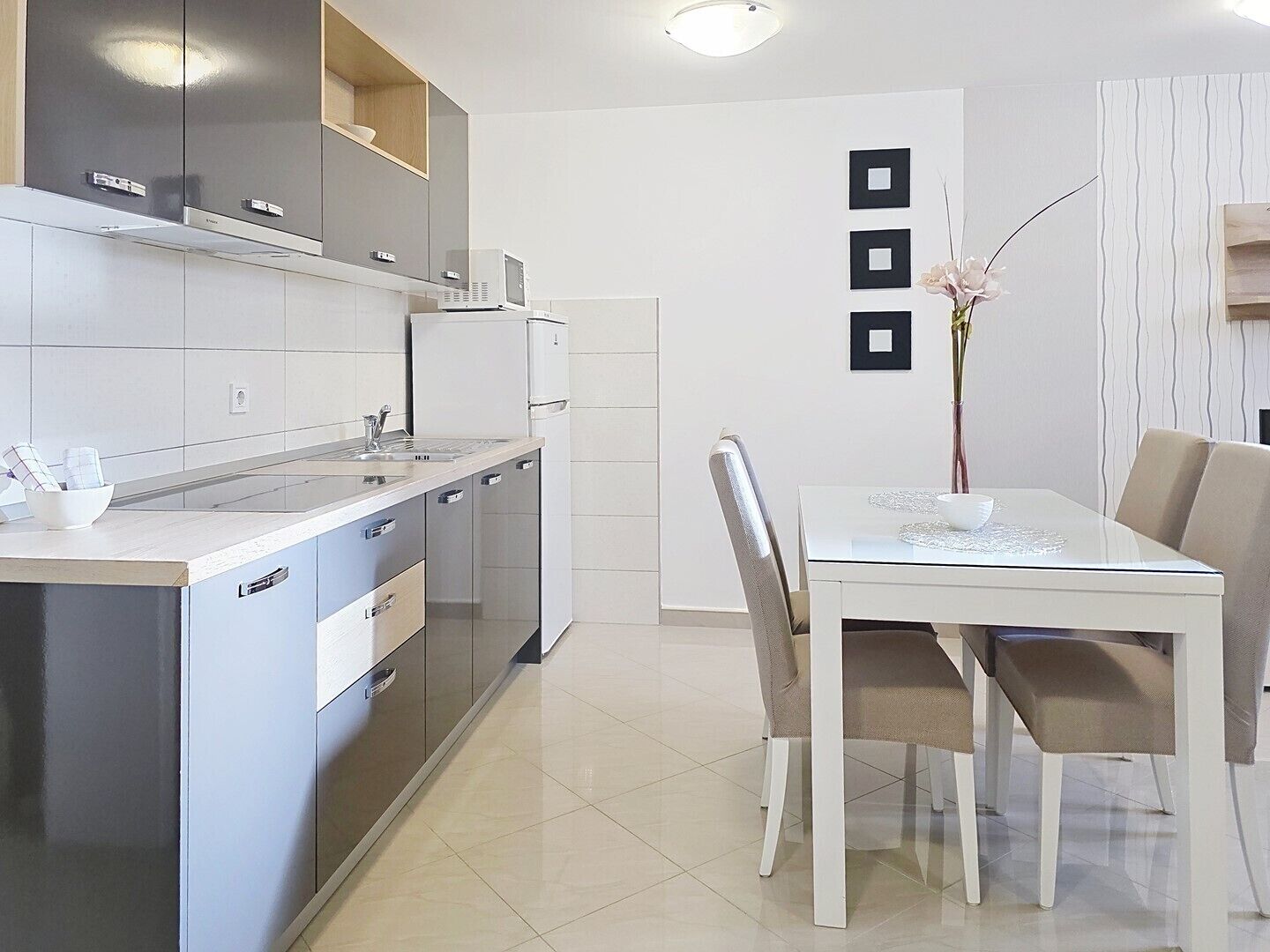 Une cuisine moderne avec un coin repas, dotée d’appareils électroménagers en acier inoxydable, d’un plan de travail blanc et d’une table à manger avec des chaises.