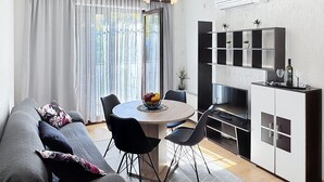 A modern living room with a sofa, dining table, chairs, and a kitchen area with a cabinet and a TV.