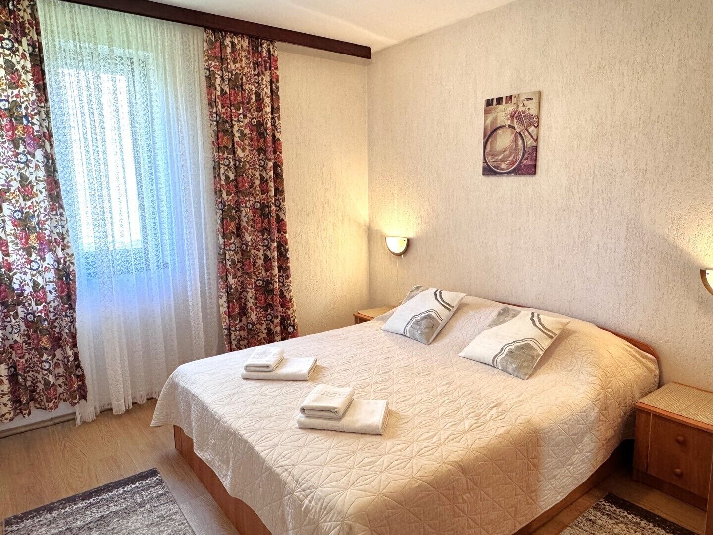 Un dormitorio con cama, cortinas, una lámpara de pared y un cuadro.