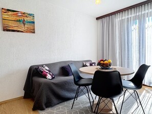Una sala de estar moderna con un sofá, dos sillones, una mesa redonda con frutero, un cuadro en la pared y un amplio ventanal con cortinas.