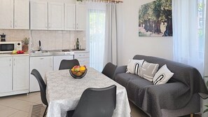 Una cocina compacta con armarios blancos, una mesa de comedor con frutero, y un sofá gris con cojines estampados.