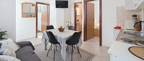 A compact living space with a dining area, kitchenette, and a TV mounted on the wall.
