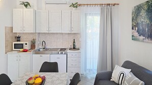 A compact kitchen with a microwave, stove, sink, and white cabinets. There's a dining table with fruit and a couch with pillows. - Apartment Grozdana No. 1A - with Terrace (Baska)