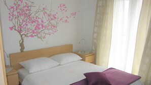 Ein Schlafzimmer mit einem Bett, einem Nachttisch, einer Lampe und einer Wanddekoration eines rosa Baumes.