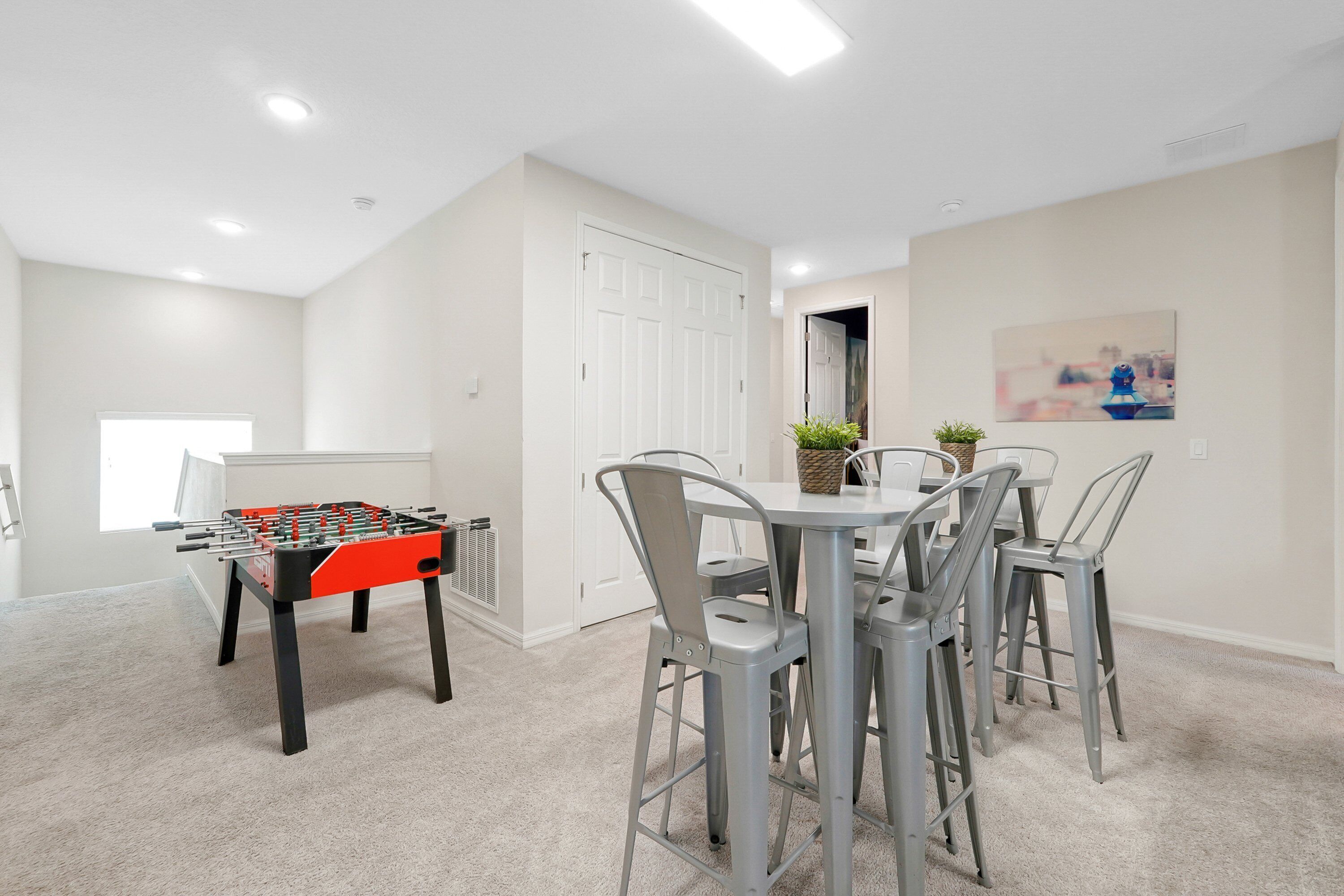 Um quarto com uma mesa de futebol de mesa, uma mesa de jantar com cadeiras e uma porta branca.