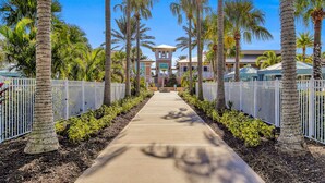 A pathway flanked by palm trees leading to a building with a central tower. - 9BR Solara Resort Near Disney | Pool, Spa & Games (Kissimmee)