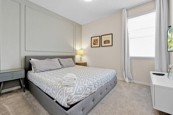 A neatly arranged bedroom with a bed, bedside table, lamp, and a window with curtains. - 9BR Solara Resort Near Disney | Pool, Spa & Games (Kissimmee)