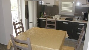 Cocina compacta con refrigerador, pileta y comedor con mesa y sillas.