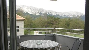 Un balcón con una mesa redonda y sillas, con vista a un paisaje montañoso.
