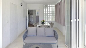 Un espace de vie compact comprenant un canapé, une table à manger avec des chaises, un petit coin cuisine et une vue par une fenêtre à carreaux.