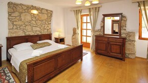 Une chambre avec un mur en pierre, un lit en bois, une commode et un miroir.