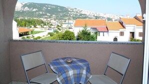 A balcony with two chairs and a table, overlooking a town with buildings and a mountain in the background.