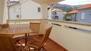 Een balkon met een houten tafel en stoelen, met uitzicht op een woongebied met terracotta daken en een berg op de achtergrond.