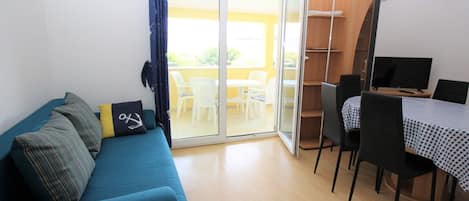Ein Wohnbereich mit einer Couch, einem Esstisch mit Stühlen und einer Glastür zum Balkon.