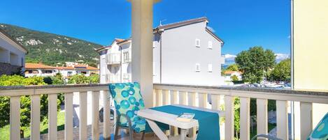 A balcony with a table and chairs, overlooking a residential area with houses and a mountain.