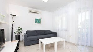 A modern living room with a grey sofa, a white coffee table, a TV, and a plant. - Apartment Lavendel - with Balcony, 250 m from the Beach (Baska)
