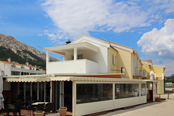 A two-story building with a balcony, large windows, and outdoor seating area.