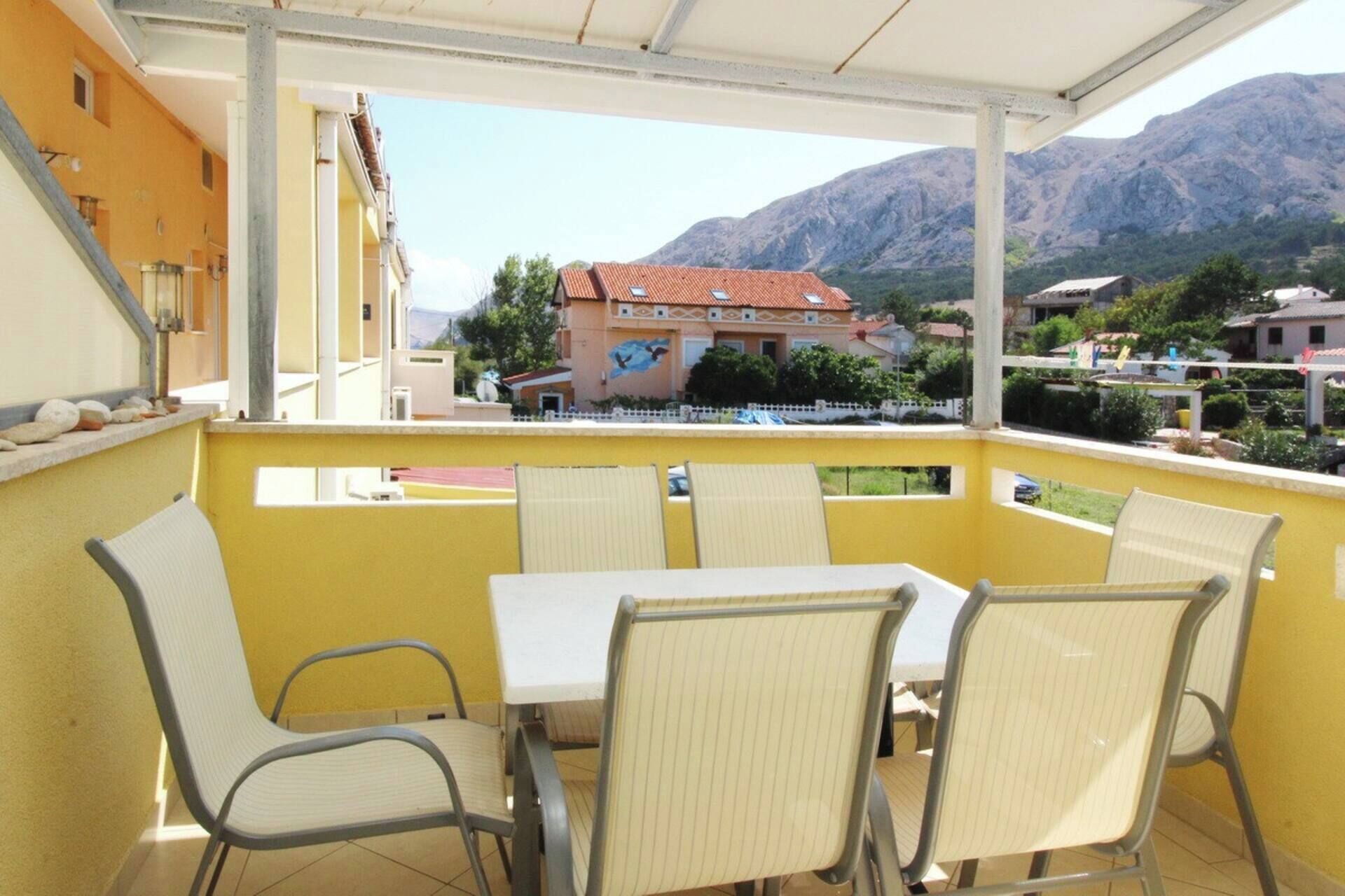 A balcony with a table and chairs, overlooking a mountain and a building with a mural.