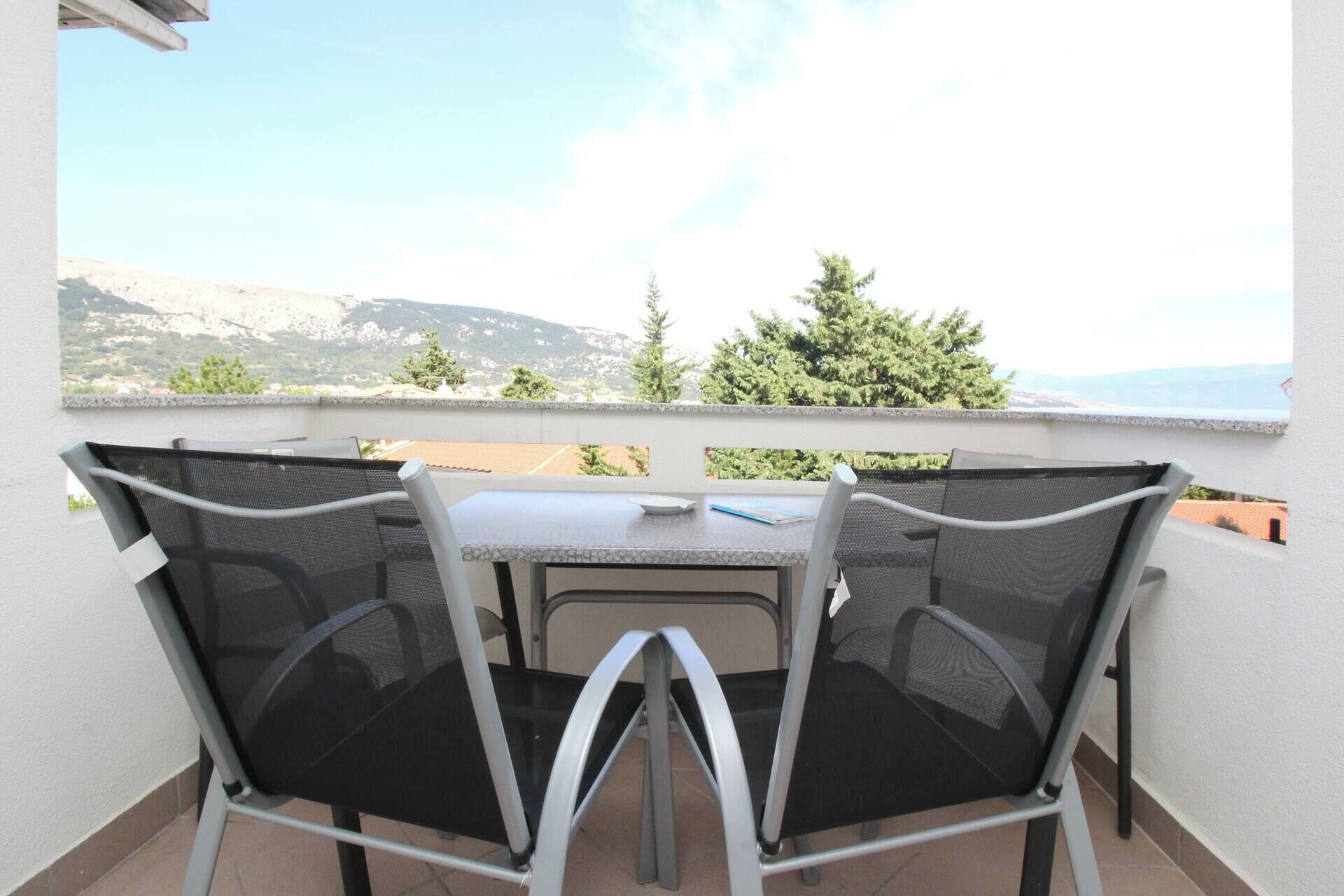 A balcony with two chairs and a table, overlooking a mountainous landscape.