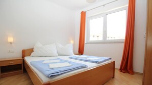 A double bed with a wooden frame, two nightstands, a window with orange curtains, and a wall-mounted light. - Apartments Mikulan Nara Priz - with Terrace, 350 m from the Beach (Baska)