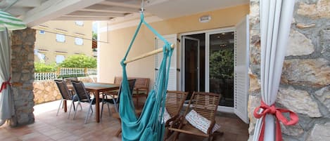 A patio with a hanging hammock, wooden chairs, and a table.