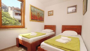 A hotel room with two wooden beds, white linens, green towels, and a painting on the wall. - Apartment Mrkus brdo - with Balcony, near the Beach (Baska)