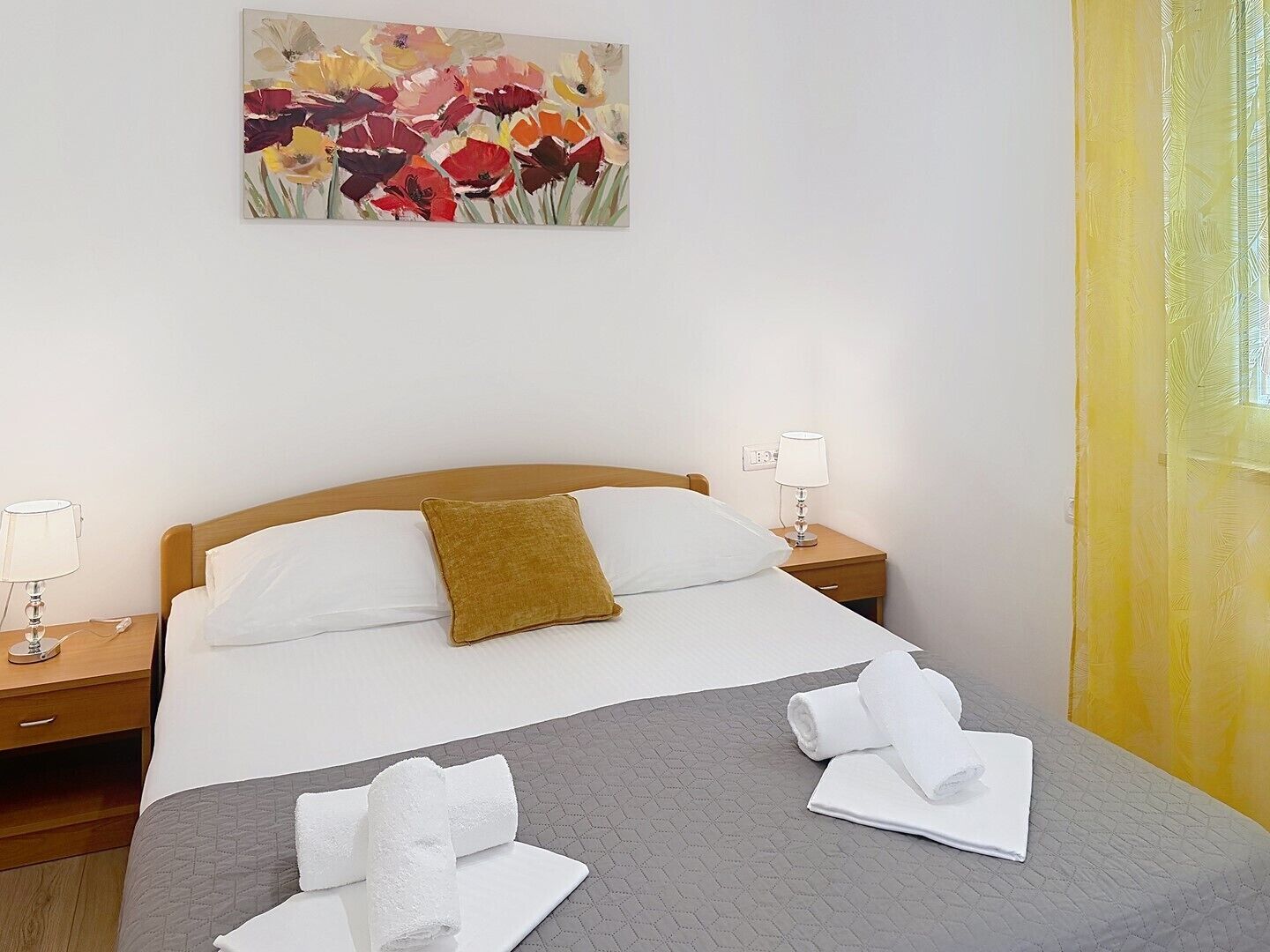 A hotel room with a bed, two bedside tables, a painting, and towels on the bed.