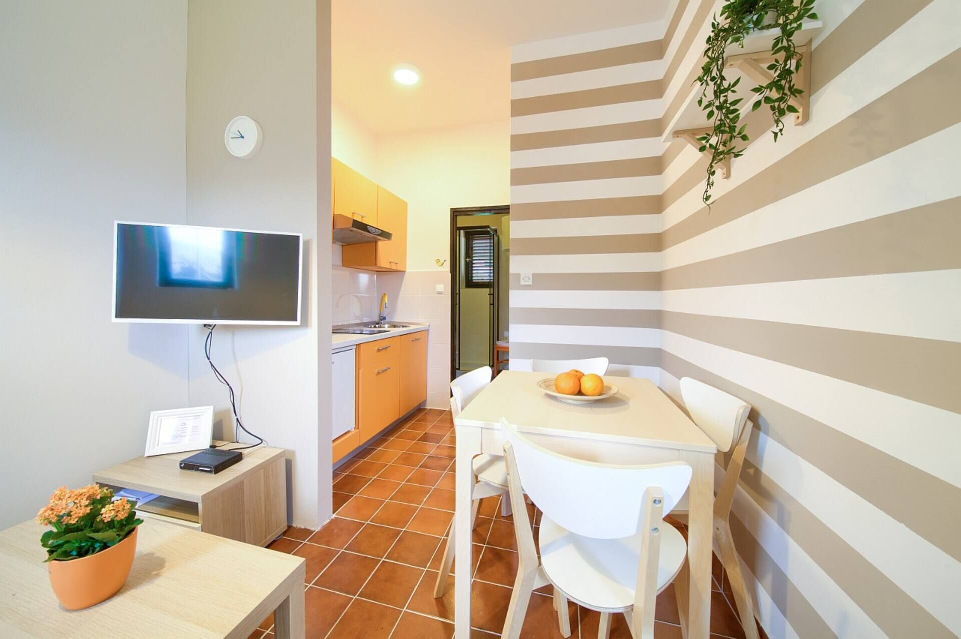 A compact kitchen with a TV, a dining table with chairs, and a striped wall.