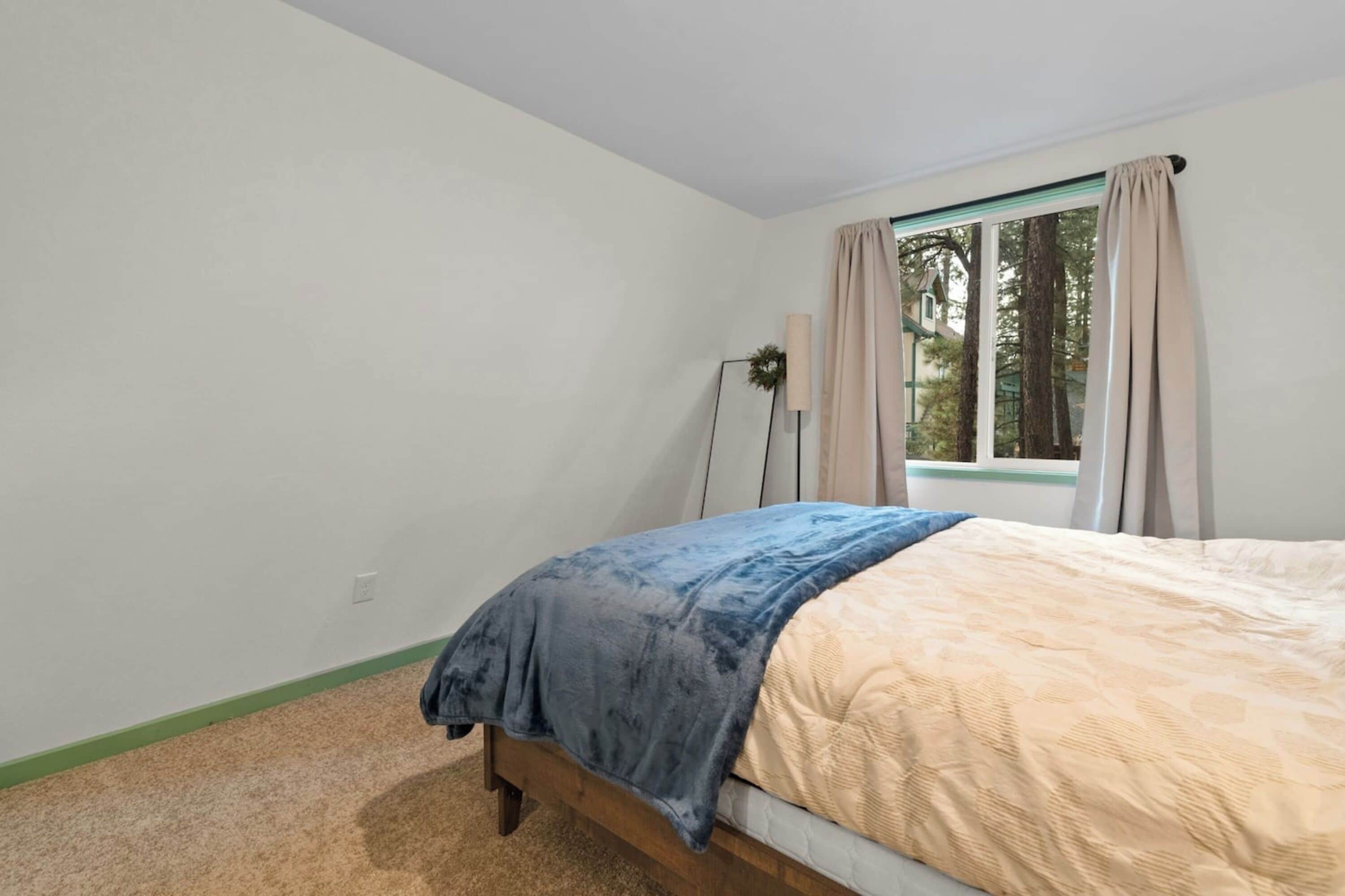 A bedroom with a bed, a window with curtains, a floor lamp, and a green-painted wall.