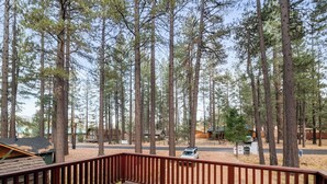 A wooden deck with a metal railing overlooking a campground with tall pine trees and several cabins. - Charming Cabin Escape (Big Bear Lake)