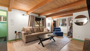 A cozy living room with a wooden ceiling, a beige sofa, a blue armchair, and a coffee table. - Charming Cabin Escape (Big Bear Lake)