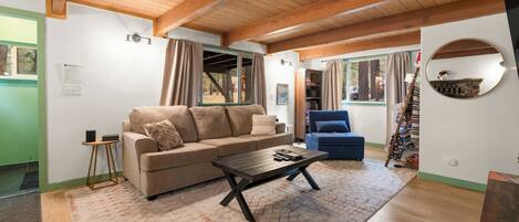 Un salón acogedor con techo de madera, un sofá color beige y un sillón azul, junto a una mesa de centro.