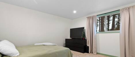 Ein Schlafzimmer mit Bett, Kommode, Fernseher und einem Fenster mit Vorhängen.