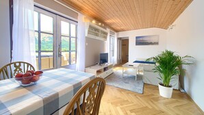 A room with a wooden ceiling, a dining table with a checkered tablecloth, a potted plant, and a sofa. - Apartment Nana K2 - with Sea View and private BBQ (Baska)
