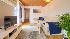 A living room with a television, a white sofa with blue cushions, a small table, and a plant. - Apartment Nana K2 - with Sea View and private BBQ (Baska)