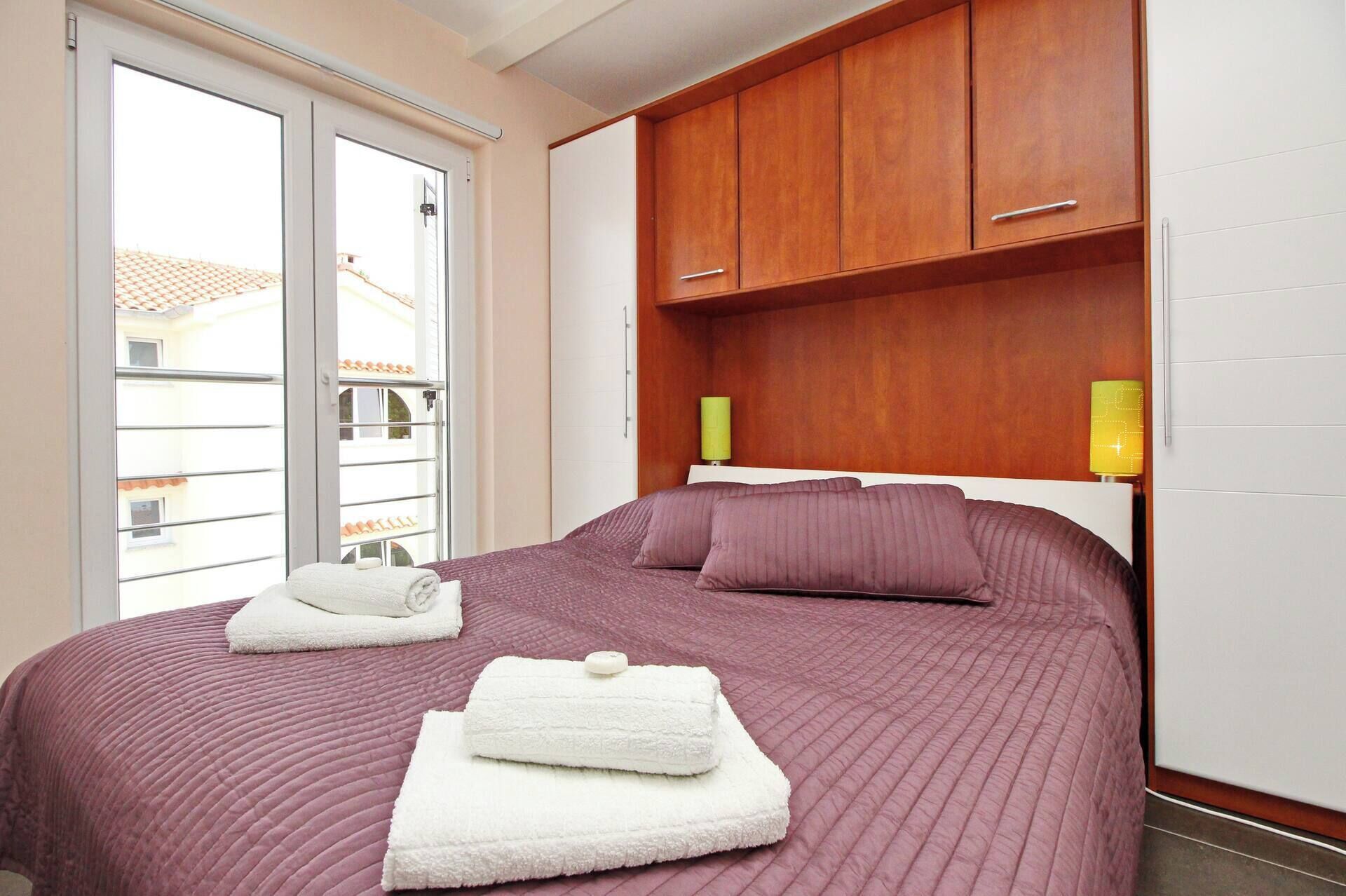 Ein Schlafzimmer mit einem großen Bett, Holzschränken und einem Fenster mit Blick auf Gebäude.