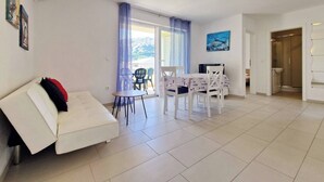Ein modernes Wohnzimmer mit einem weißen Sofa, einem Esstisch mit Stühlen und Blick durch eine Glastür ins Freie.