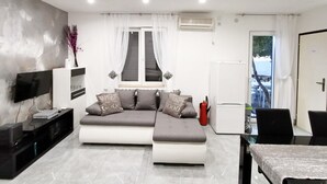 Una sala moderna con un sofá, un televisor, una mesa de comedor y un ventanal con cortinas.