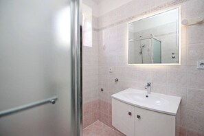 A modern bathroom with a glass shower enclosure, a white sink, and a large mirror above the sink. - Apartment Lana priz - near the Center and the Beach (Baska)