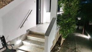 Una escalera que lleva a una puerta, un banco y una planta en maceta.