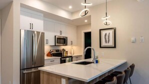 A modern kitchen with stainless steel appliances, a central island, and pendant lighting. - Cosmo’s Getaway | Mtn Views | AC | BBQ | King Bed (Golden)