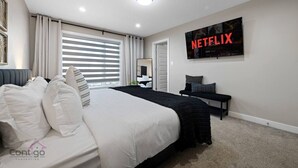 A modern bedroom with a large bed, a TV mounted on the wall, and a window with blinds.
