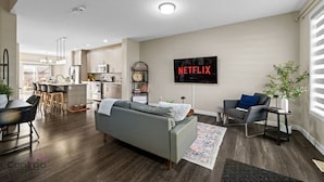 A modern living room with a grey sofa, a coffee table, and a TV mounted on the wall displaying 'NETFLIX'.