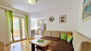 A living room with a sofa, a coffee table, and a dining table. There is a kitchen in the background with cabinets and a microwave.